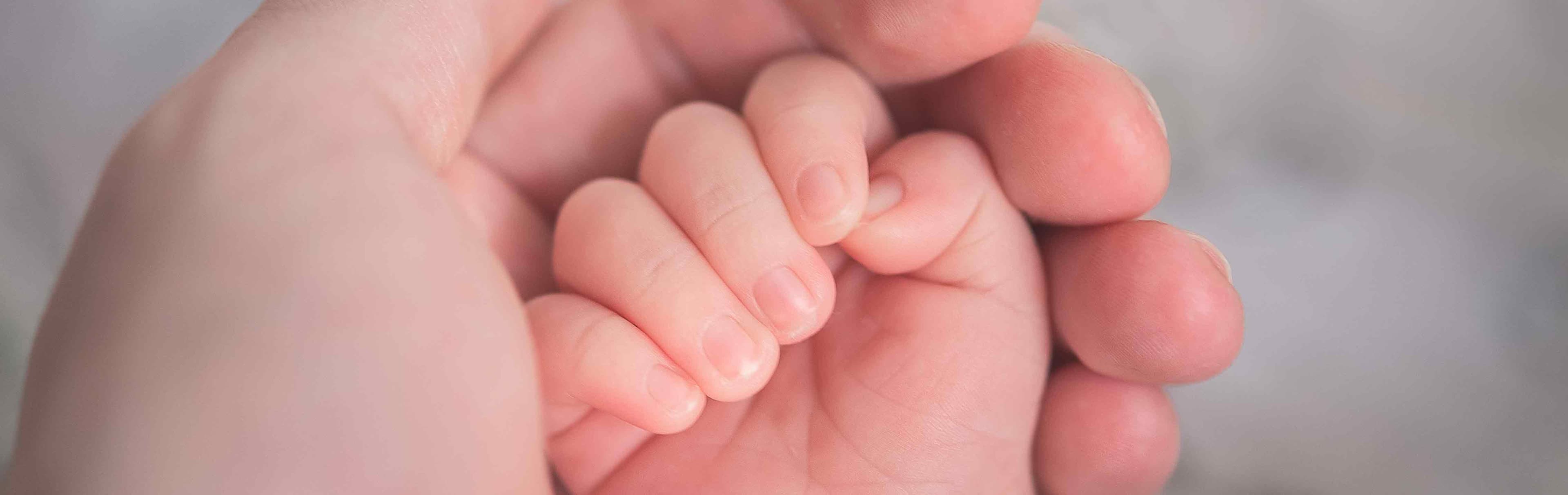 En bäbis hand omgiven av en större hand